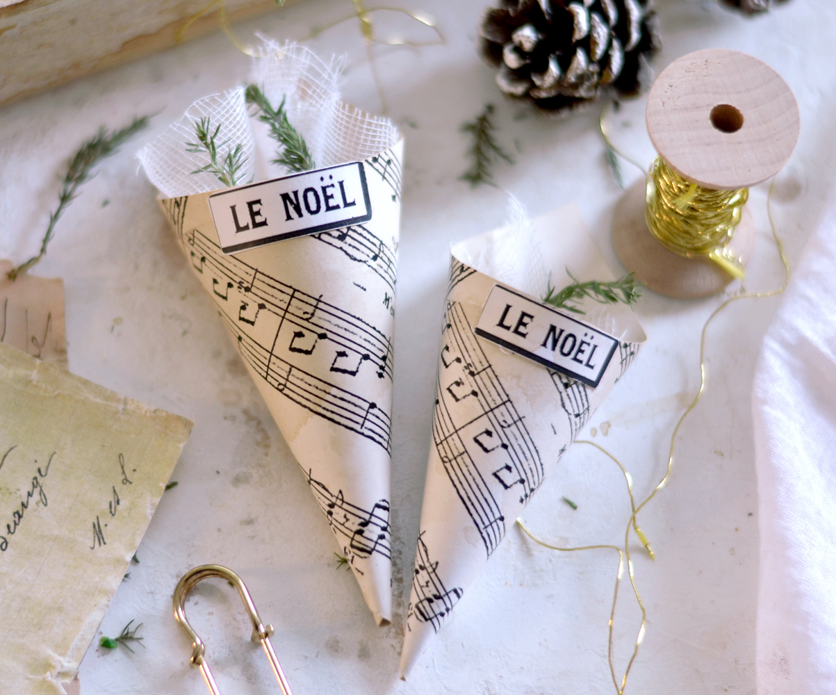 Two paper cones laying on the table with gold metallic thread, vintage paper, a pine cone and a gold safety pin